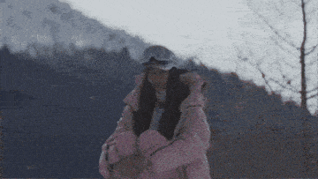 a woman in a pink jacket and goggles stands in front of a mountain