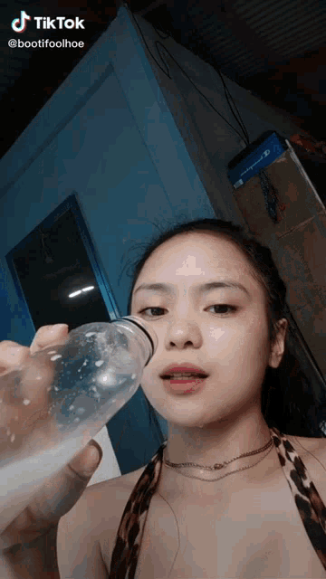 a woman drinking from a clear plastic bottle with a tiktok logo above her