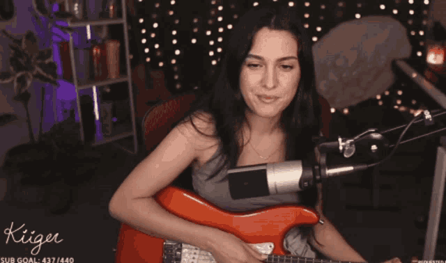 a woman playing a guitar in front of a microphone with the word kiiger on the bottom right