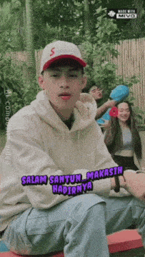a young man wearing a supreme hat says " salam santun makasih "
