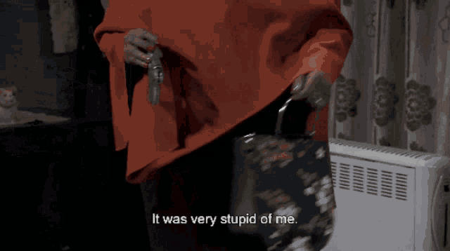 a woman in an orange poncho is holding a purse and says it was very stupid of me