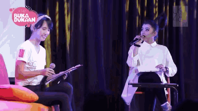a woman singing into a microphone with a sign that says buka bukaan behind her