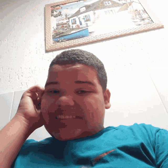a boy in a blue shirt is smiling in front of a framed picture on the wall