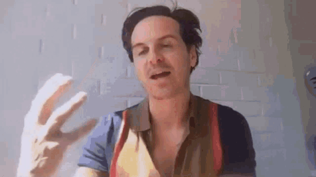 a man in a colorful shirt is talking on a video call while waving his hand .