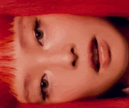 a close up of a woman 's face with red hair and white eye shadow .