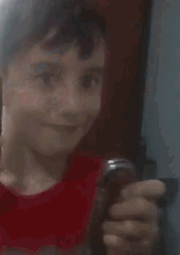 a boy in a red shirt is holding a cell phone .