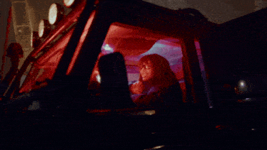 a woman with glasses is sitting in a car with a red light behind her