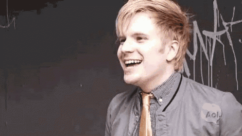 a man wearing a jacket and tie is laughing in front of a chalkboard .
