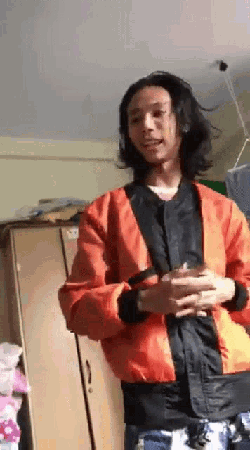 a man with long hair is wearing a red jacket and holding a glass of water .