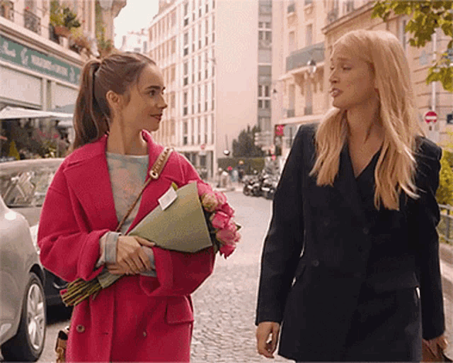 a woman in a pink coat is holding a bouquet of flowers next to another woman