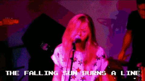a woman singing into a microphone with the words " the falling sun burns a line " below her