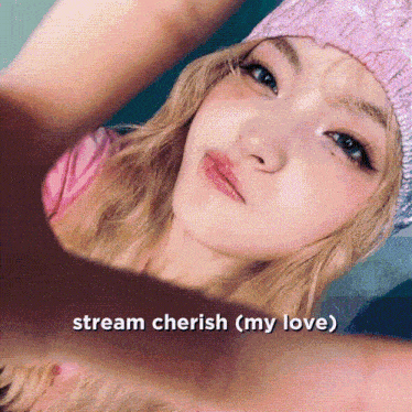 a woman wearing a pink hat is making a heart shape with her hands and the words stream cherish ( my love ) below her
