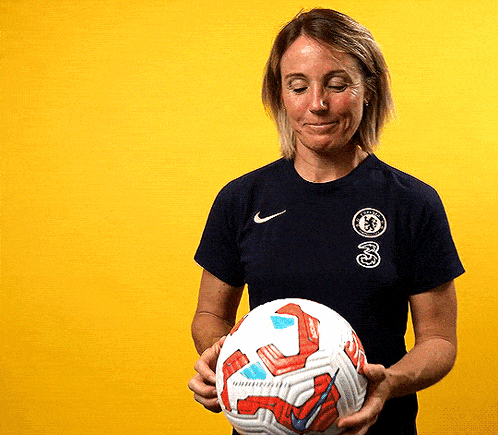 a woman in a nike shirt holds a soccer ball in front of a yellow background