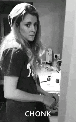 a black and white photo of a woman standing in front of a sink in a kitchen .