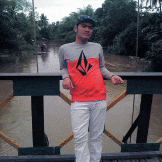 a man wearing a volcom shirt stands on a bridge over water