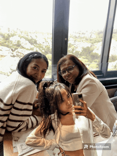 a woman taking a selfie with two other women in front of a window that says photoroom at the bottom