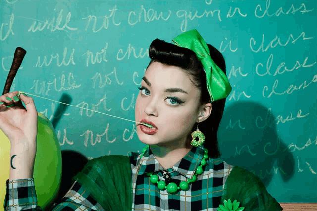 a girl with a green bow on her head is standing in front of a chalkboard that says i will not chew gum