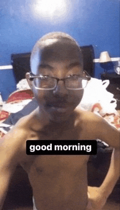 a shirtless young man wearing glasses is taking a selfie in a bedroom .