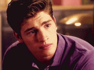 a young man wearing a purple shirt is looking at the camera .