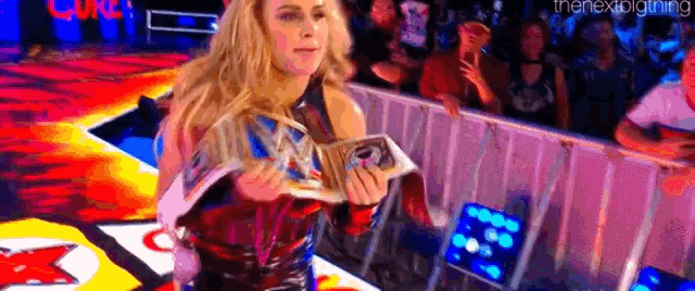 a woman is holding a trophy in front of a crowd at a wrestling event .