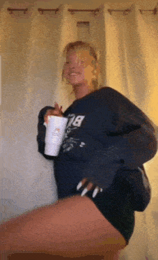 a woman in a blue sweatshirt is holding a white cup .