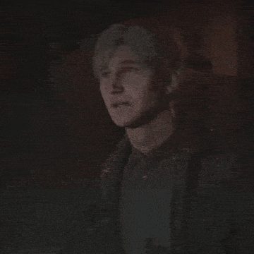 a close up of a man 's face in a dark room . he is wearing a jacket and tie .