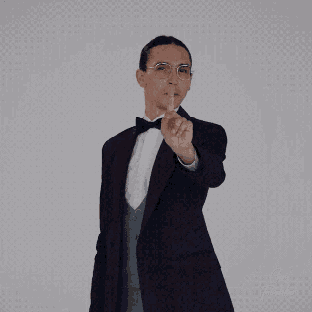 a man in a tuxedo and bow tie is pointing his finger at the camera
