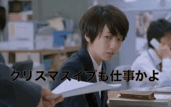 a man in a suit is sitting at a desk holding a piece of paper with japanese writing on it .