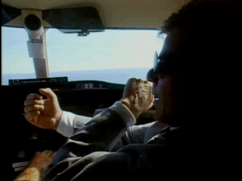 a man in a suit and tie is driving a car with his hand on the steering wheel