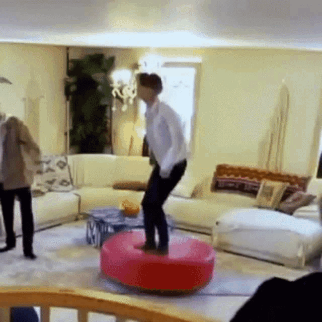 a man is standing on a red ottoman in a living room
