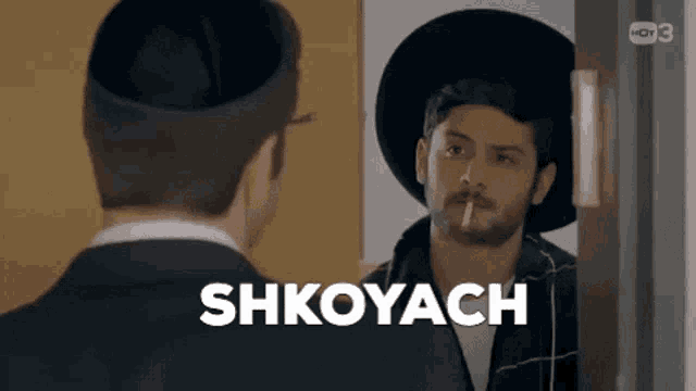 a man in a hat is smoking a cigarette while looking at himself in a mirror .