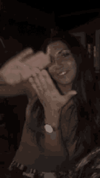 a woman wearing a watch is making a peace sign with her hands in the dark .
