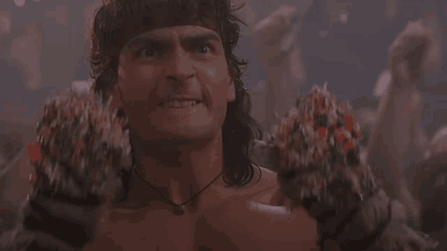 a shirtless man with a necklace around his neck holds a pair of clawed gloves
