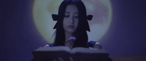 a woman is reading a book in a dark room while holding a flower .