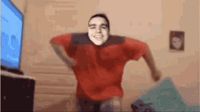 a man in a red shirt is dancing in a room in front of a tv .