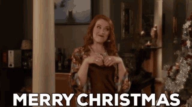 a woman is saying merry christmas in front of a christmas tree