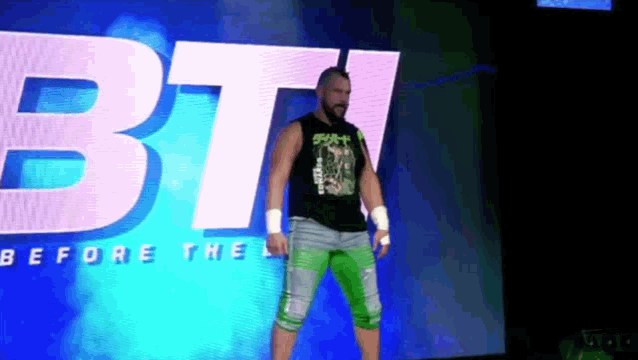 a man in a black tank top and green shorts stands in front of a large bt sign