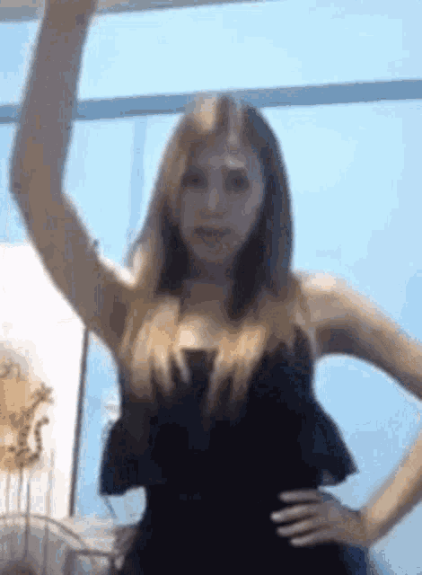 a woman in a black dress is standing in front of a blue wall with her hand in the air .