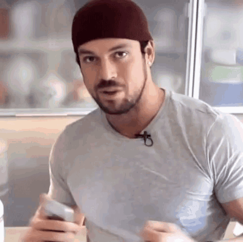 a man with a beard wearing a hat and a gray shirt is sitting at a table .