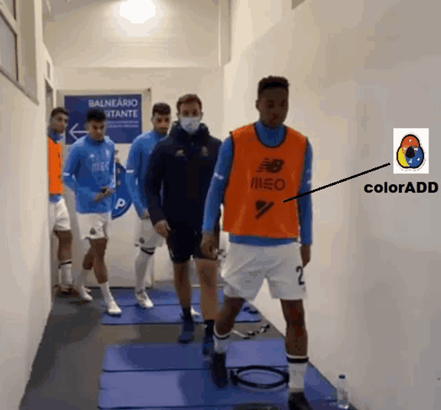 a group of soccer players are walking down a hallway and one of them is wearing an orange vest that says meo