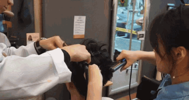 a woman is getting her hair straightened by a man in a hair salon .