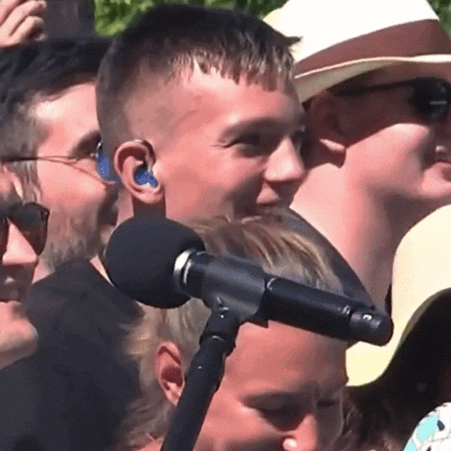 a group of people are standing around a microphone with a man wearing ear buds behind it .