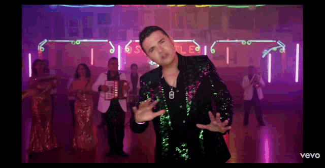 a man in a sequined jacket is standing in front of a group of people holding accordions in a video for vevo