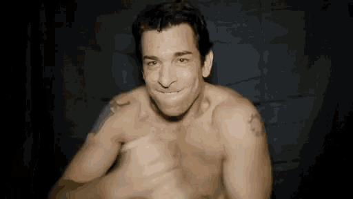 a shirtless man is smiling and making a funny face in a dark room .