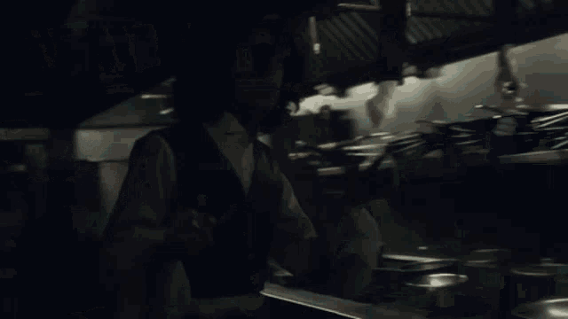 a man in a black vest and white shirt is standing in a kitchen .