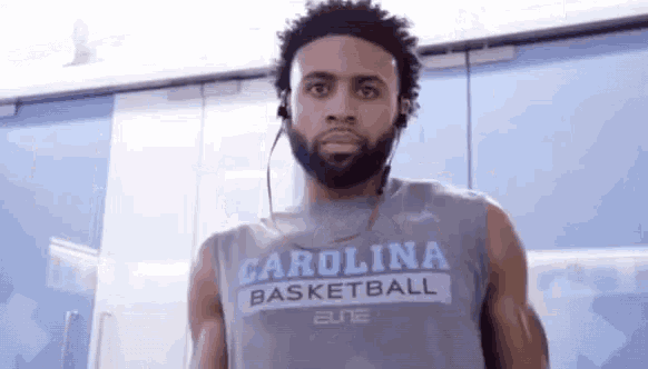 a man wearing a carolina basketball shirt and headphones is standing in a room .