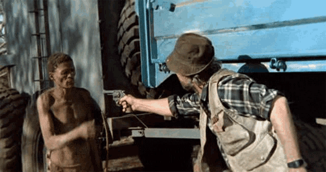 a man pointing a gun at another man in front of a truck