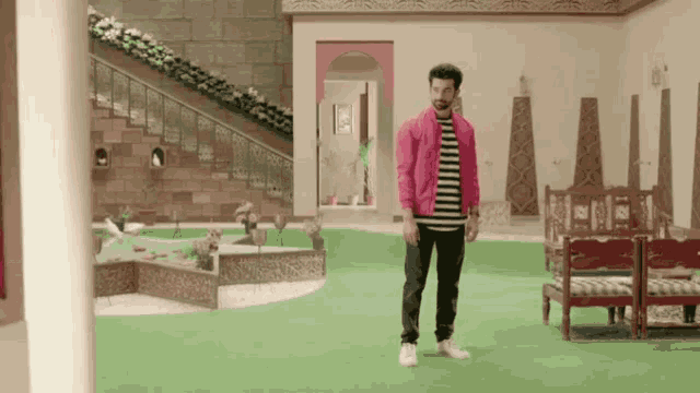 a man in a pink jacket is standing in a room with stairs