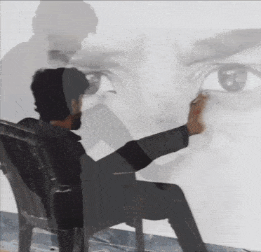 a man is sitting in a chair and drawing a picture of a man 's face