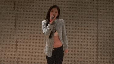 a woman is singing into a microphone in front of a perforated wall